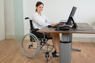Arbeiten mit Behinderung - Frau mit Rollstuhl am Schreibtisch
